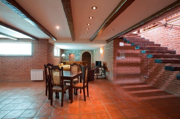 A spacious room with a brick wall, a staircase, and a dining area with wooden furniture.
