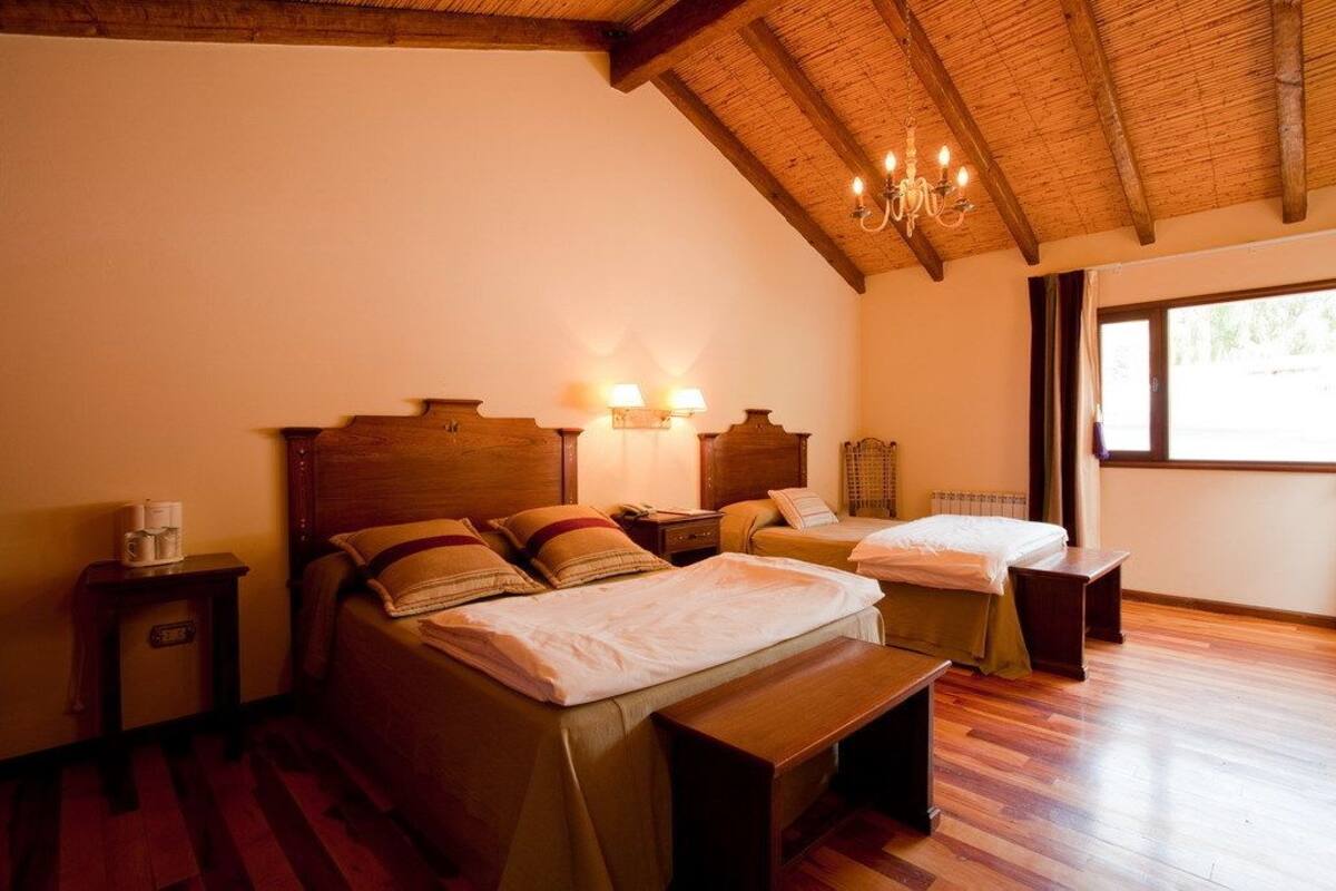 Habitación de hotel con dos camas, cabeceros de madera, un candelabro y un ventanal grande.