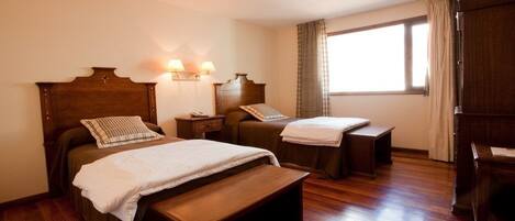 A hotel room with two beds, wooden headboards, bedside tables, and a window with curtains.