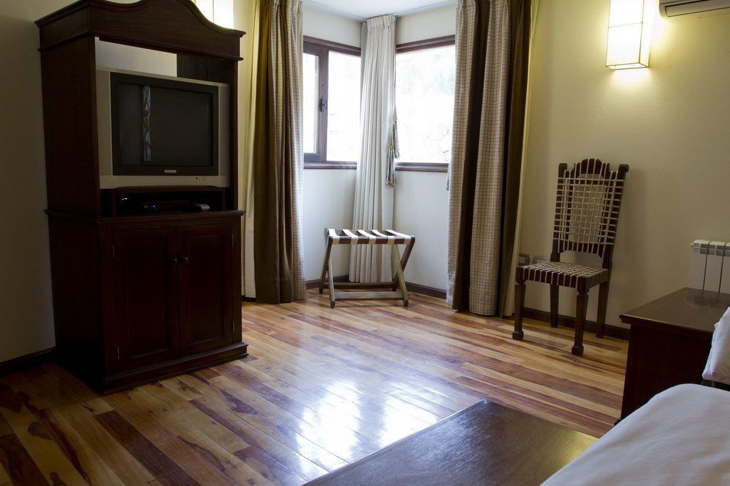 Habitación de hotel con suelo de madera, un televisor sobre un mueble, un radiador, una silla y una cama.