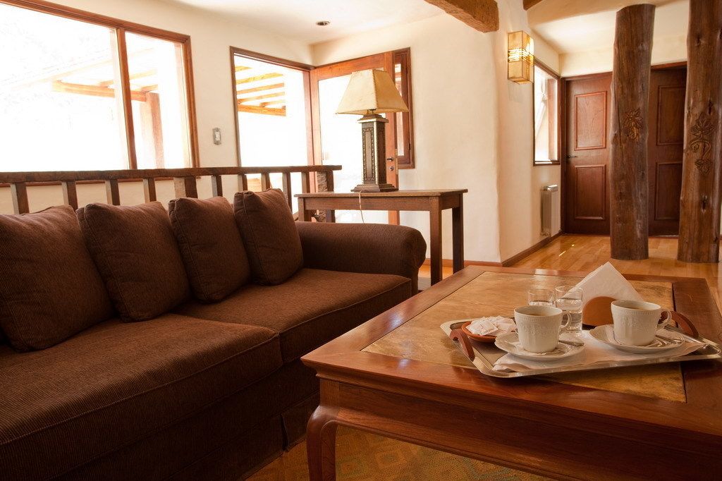 Un salón acogedor con un sofá marrón, una mesa de centro de madera con tazas y platillos, y una lámpara.