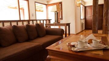 Un salón acogedor con un sofá marrón, una mesa de centro de madera con tazas y platillos, y una lámpara.