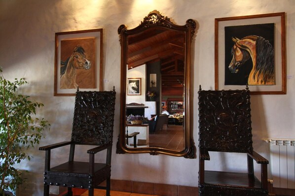 Dos sillones decorados, un espejo y dos cuadros enmarcados con motivos de caballos en la pared.
