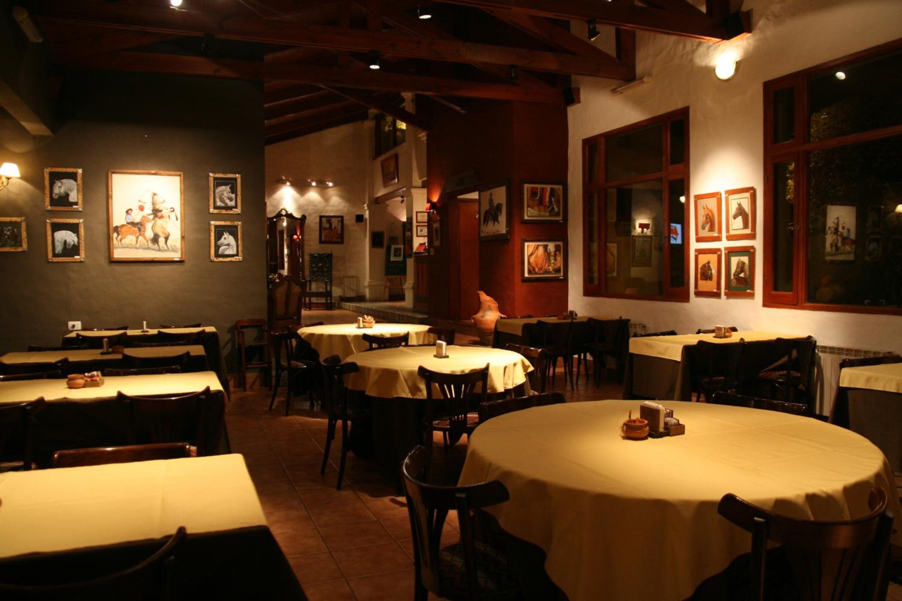 Un restaurant avec plusieurs tables rondes recouvertes de nappes jaunes, des chaises en bois et des tableaux encadrés accrochés aux murs.