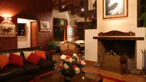 Uma sala de estar acolhedora com lareira, um sofá com almofadas vermelhas e um vaso de flores.