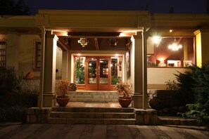 A building entrance with a set of steps leading up to a wooden door, flanked by two potted plants. - Hostería Lunahuana (Tafi del Valle)