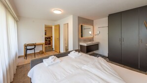 Hotellihuone, jossa on suuri sänky, työpöytä, peilillä varustettu meikkipöytä ja vaatekaappi.