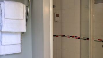 Un baño con inodoro, ducha con puerta de cristal y toallero con toallas dobladas.