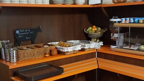 A breakfast bar with stacked plates, a basket of bread, and a coffee machine. - Delfotel (Hautefond)