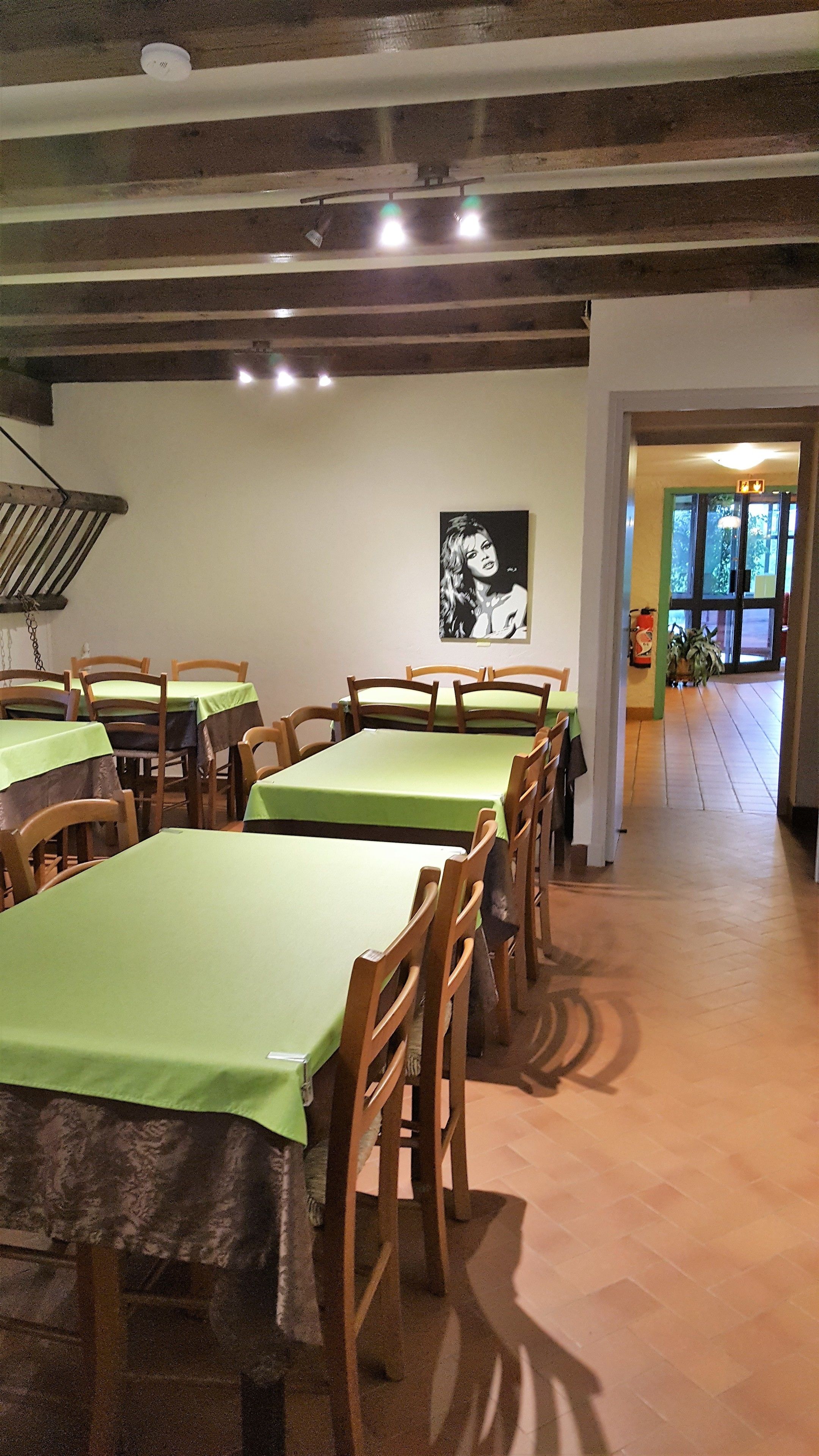 A dining area with multiple tables and chairs, wooden beams on the ceiling, and a framed picture on the wall.