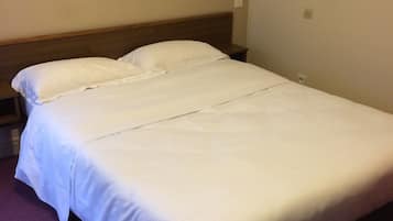 Una cama individual con ropa de cama blanca en una habitación con paredes color crema y una alfombra morada.