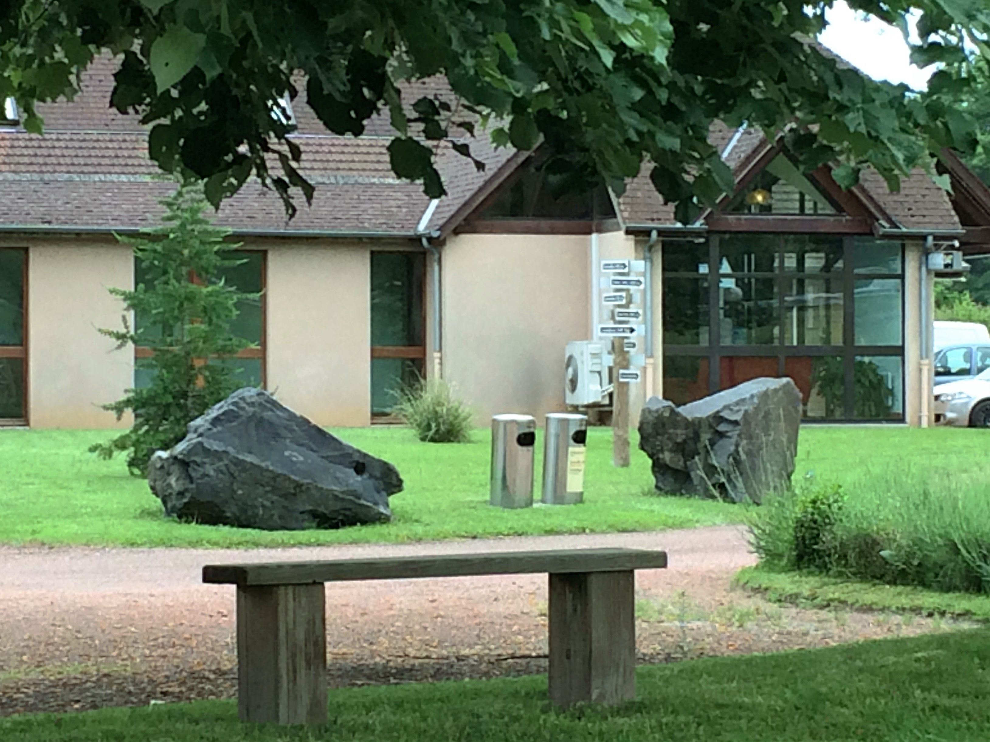 A building with a stone facade, large rocks, and a wooden bench in a landscaped area.