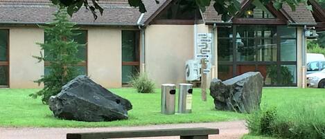 Un edificio con fachada de piedra, grandes rocas y un banco de madera en un área ajardinada.