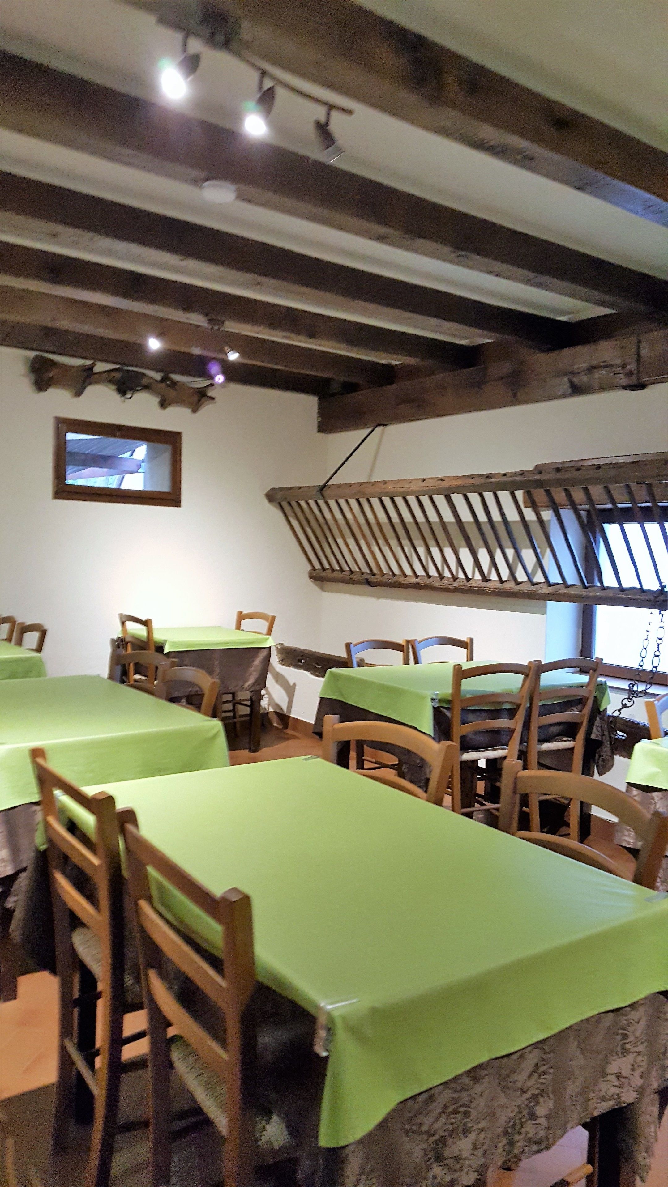 A dining area with wooden tables and chairs, a rustic ceiling with exposed beams, and a hanging light fixture.