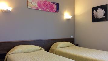 Ein Hotelzimmer mit zwei Einzelbetten, einem Holzkopfteil, einem Blumenbild und Wandleuchten.