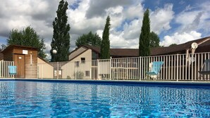 A swimming pool with clear water, surrounded by a white fence, and a wooden building with a sign indicating a WC. - Delfotel (Hautefond)