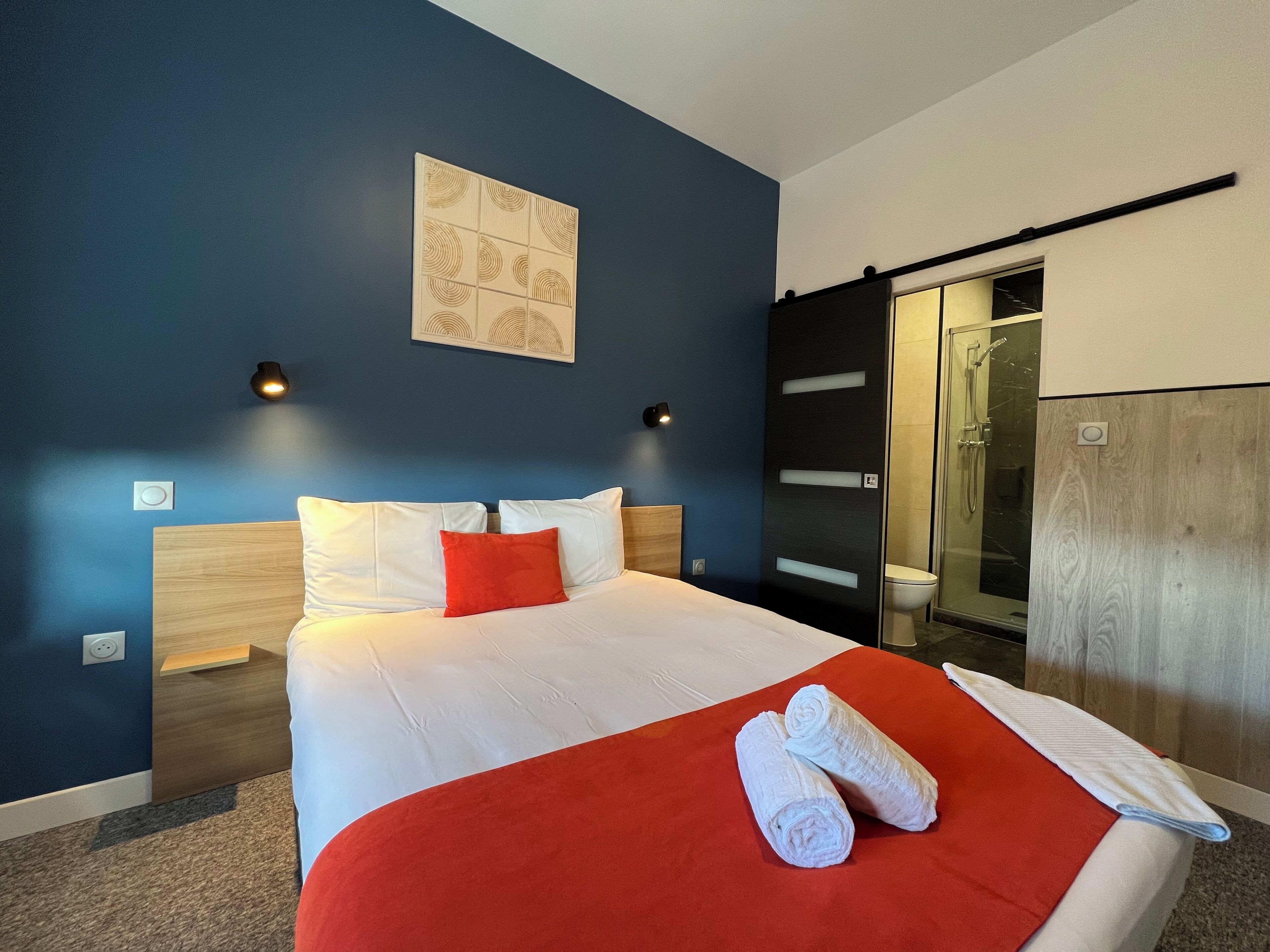 Habitación de hotel moderna con una cama grande, una manta roja y dos toallas enrolladas.