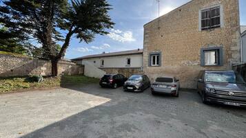 A parking area with three cars, a stone building, and a tree.