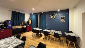 A dining area with tables and chairs, a coffee machine, and a counter with a plant.