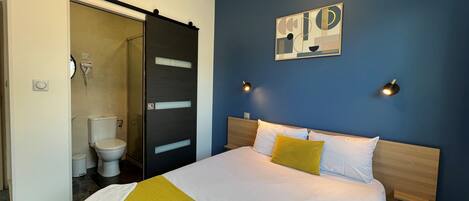 A hotel room with a bed, a bathroom, and a blue wall with a painting.