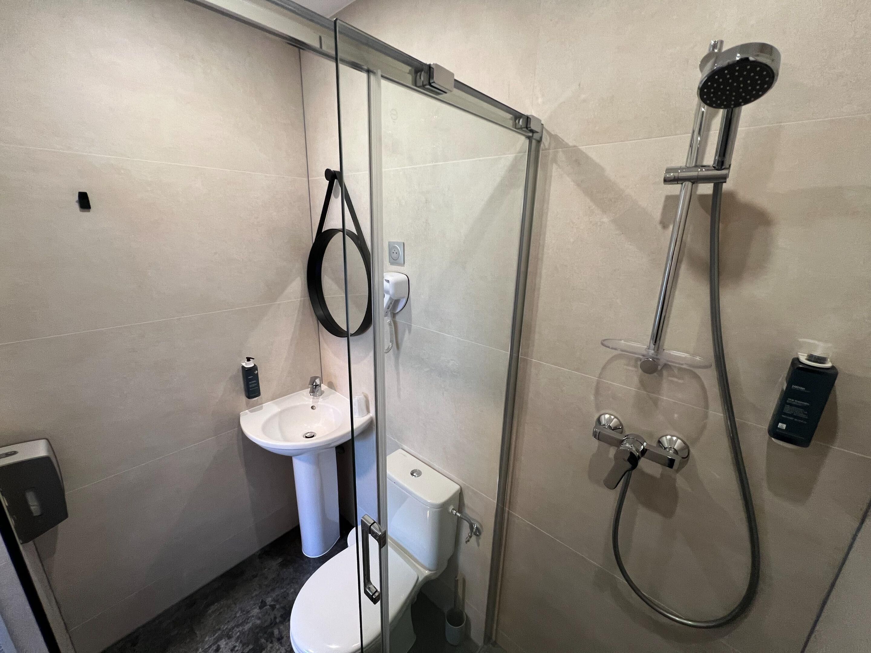 Un baño moderno con ducha envuelta en vidrio, lavamanos pedestal blanco y un inodoro.