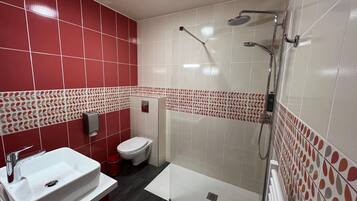 A bathroom with a white sink, red tiled walls, a toilet, and a shower area.