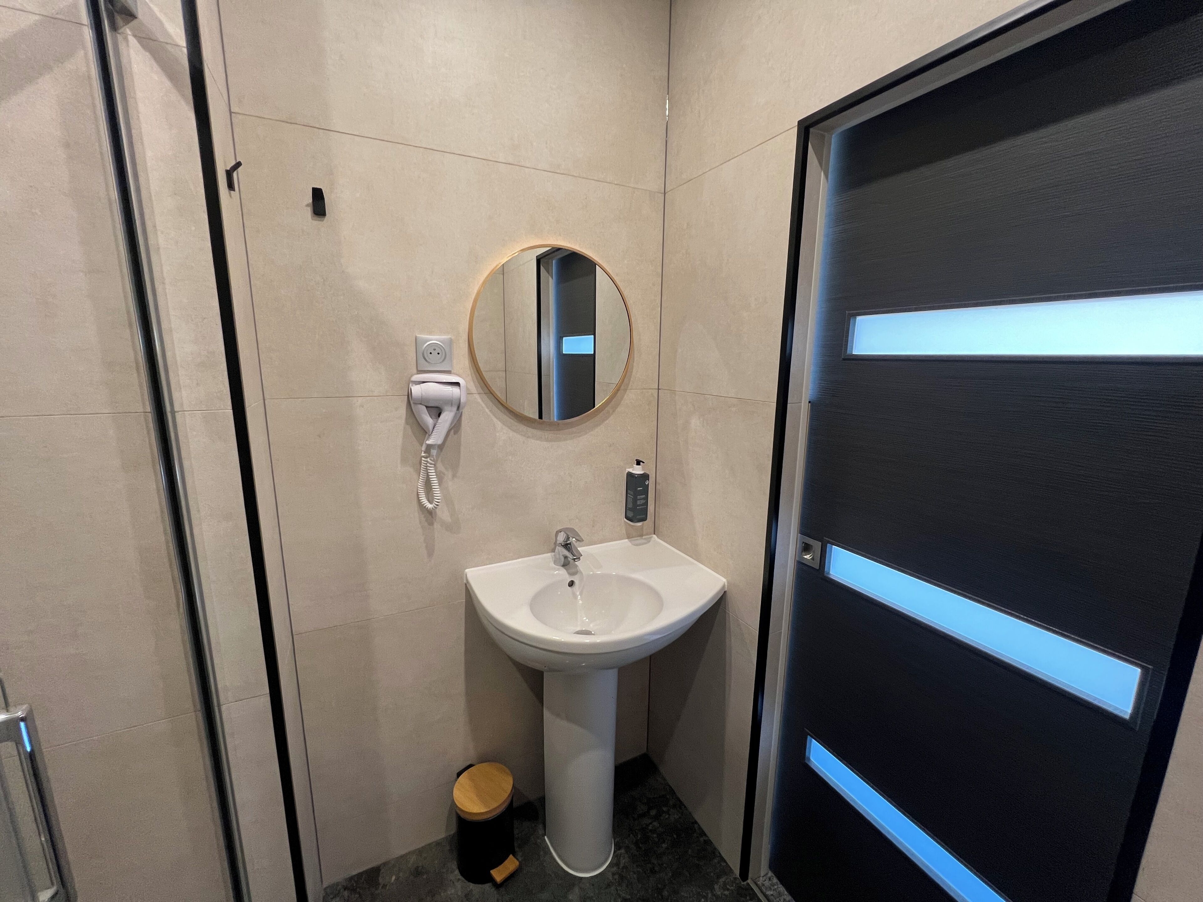 A modern bathroom with a white sink, a mirror, and a trash bin.