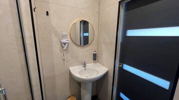 A modern bathroom with a white sink, a mirror, and a trash bin.