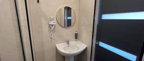 A modern bathroom with a white sink, a mirror, and a trash bin.