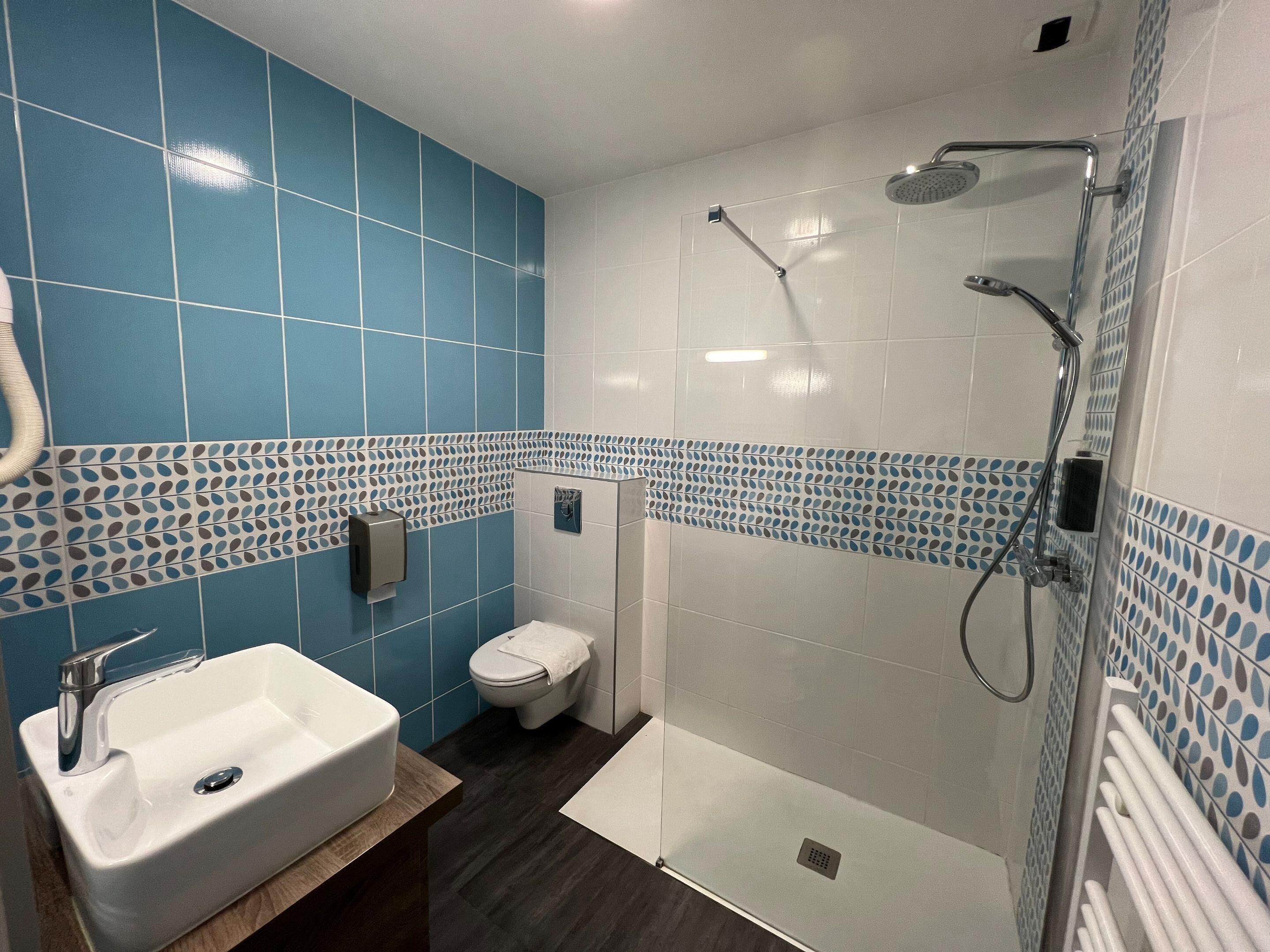 A bathroom with a white sink, blue tiled walls, a toilet, and a glass-enclosed shower area.
