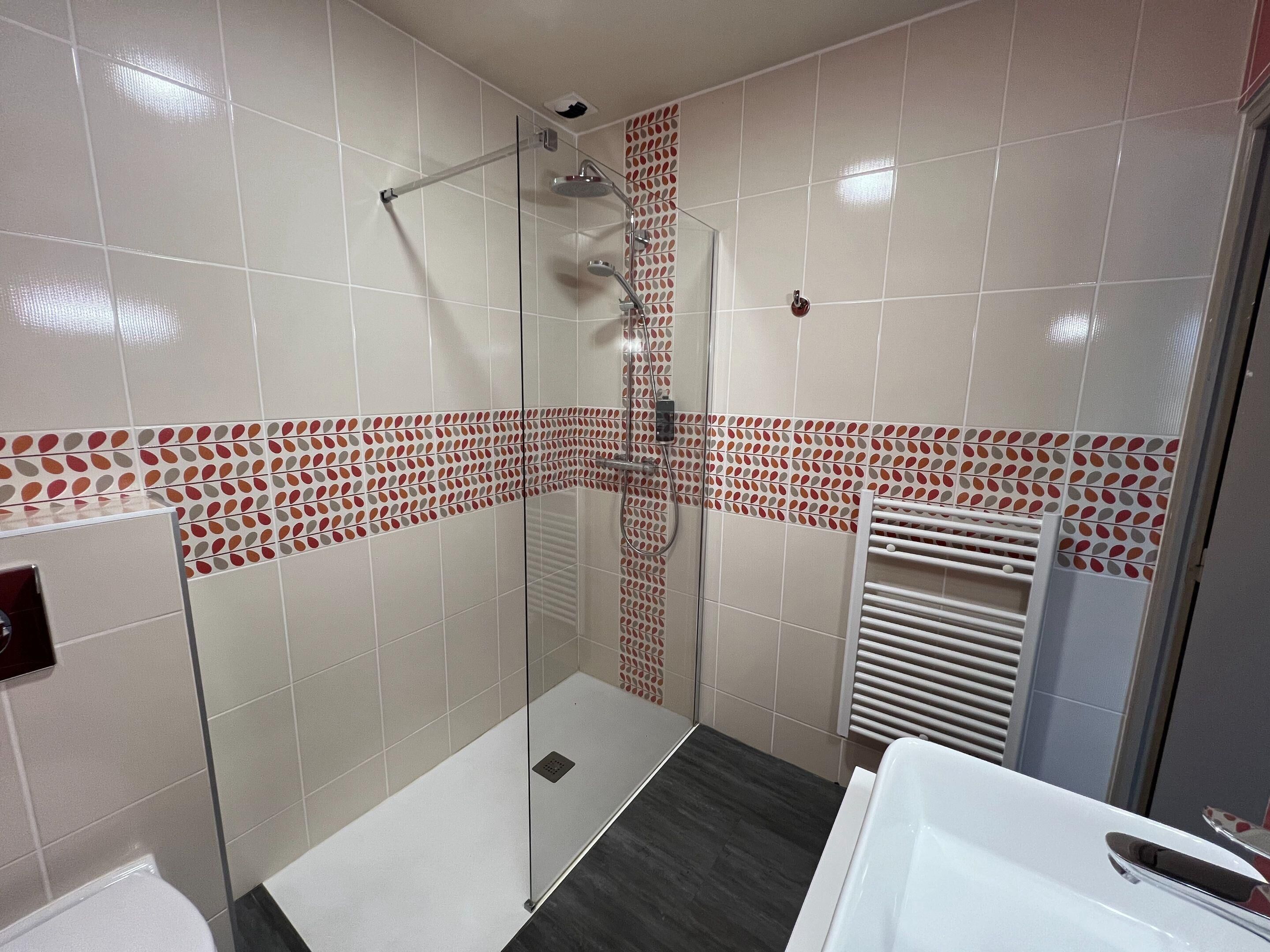Een moderne badkamer met een douchecabine van glas, een witte badkuip en behangtegels op de wanden.