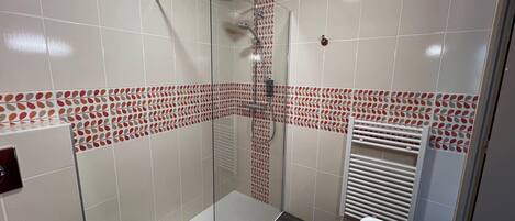 A modern bathroom with a glass shower enclosure, a white bathtub, and patterned tiles on the walls.