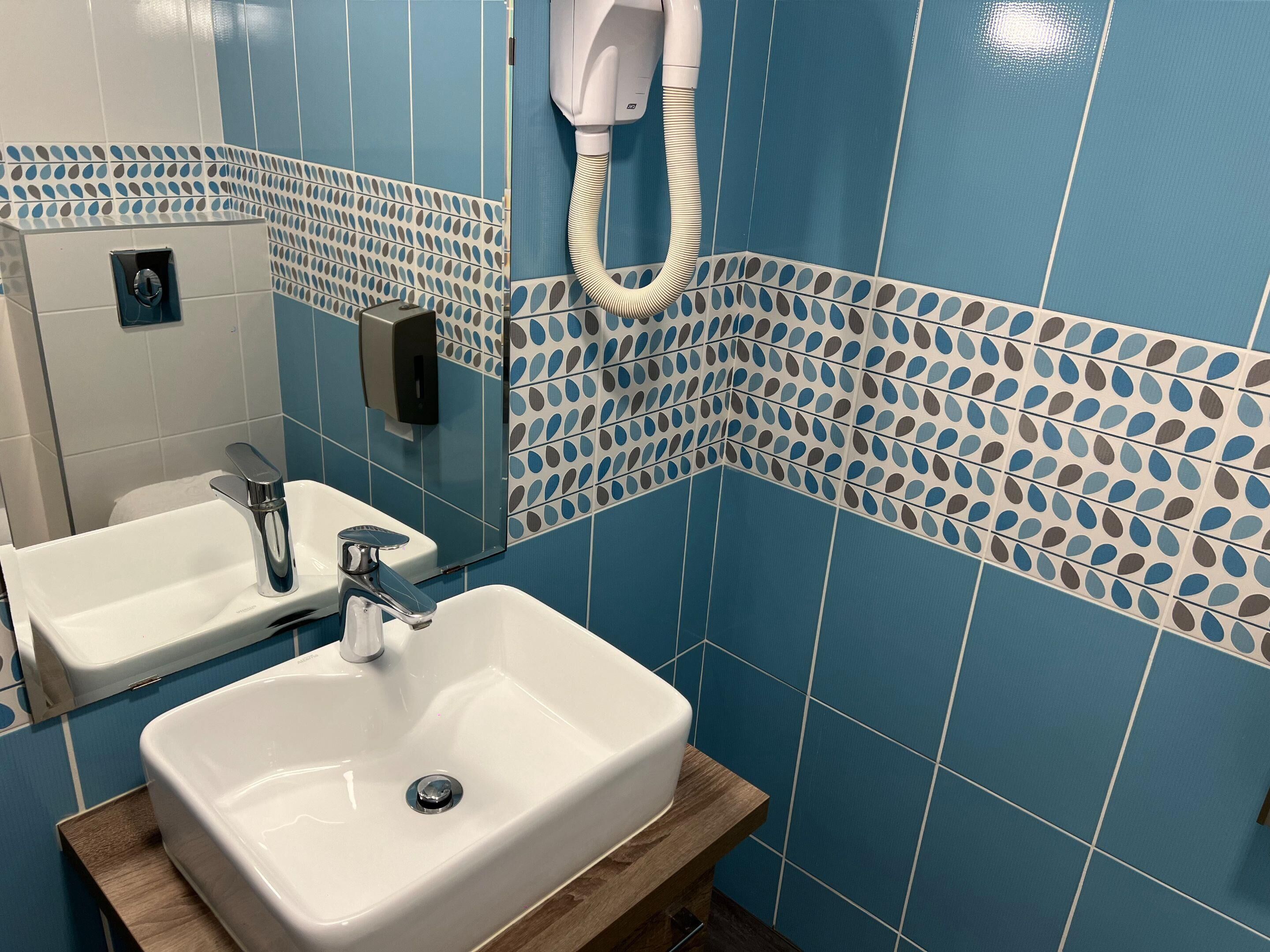 A bathroom with two sinks, a mirror, and a hairdryer mounted on the wall.