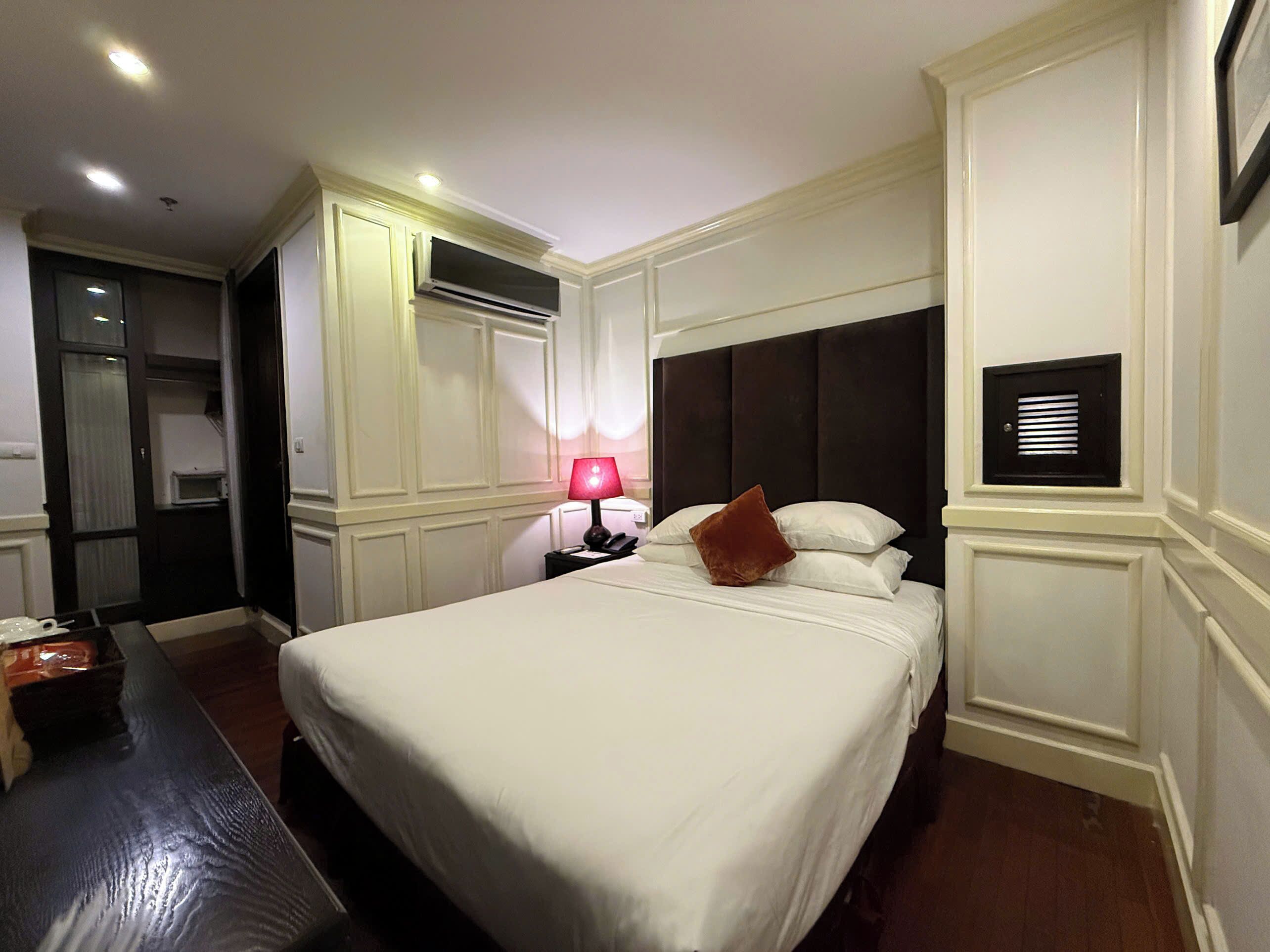 Une chambre d’hôtel avec un grand lit, une table de chevet avec une lampe, un appareil de climatisation, une armoire et une petite fenêtre.