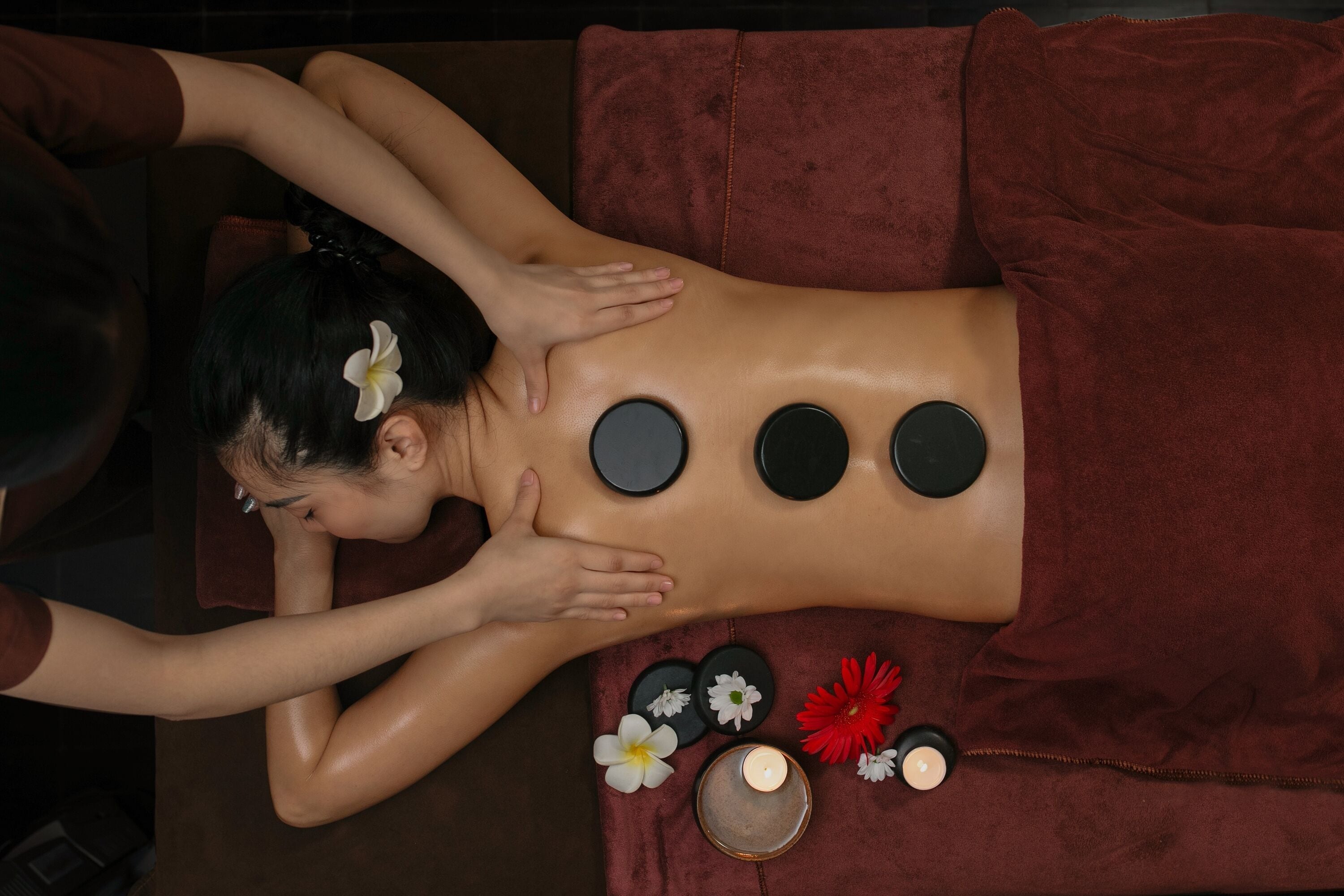 A person receiving a back massage with circular stones and flowers on a red towel.