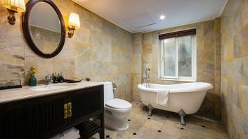 Une salle de bain comprenant une baignoire sur pieds, des toilettes, un meuble-lavabo avec un miroir et des appliques murales.