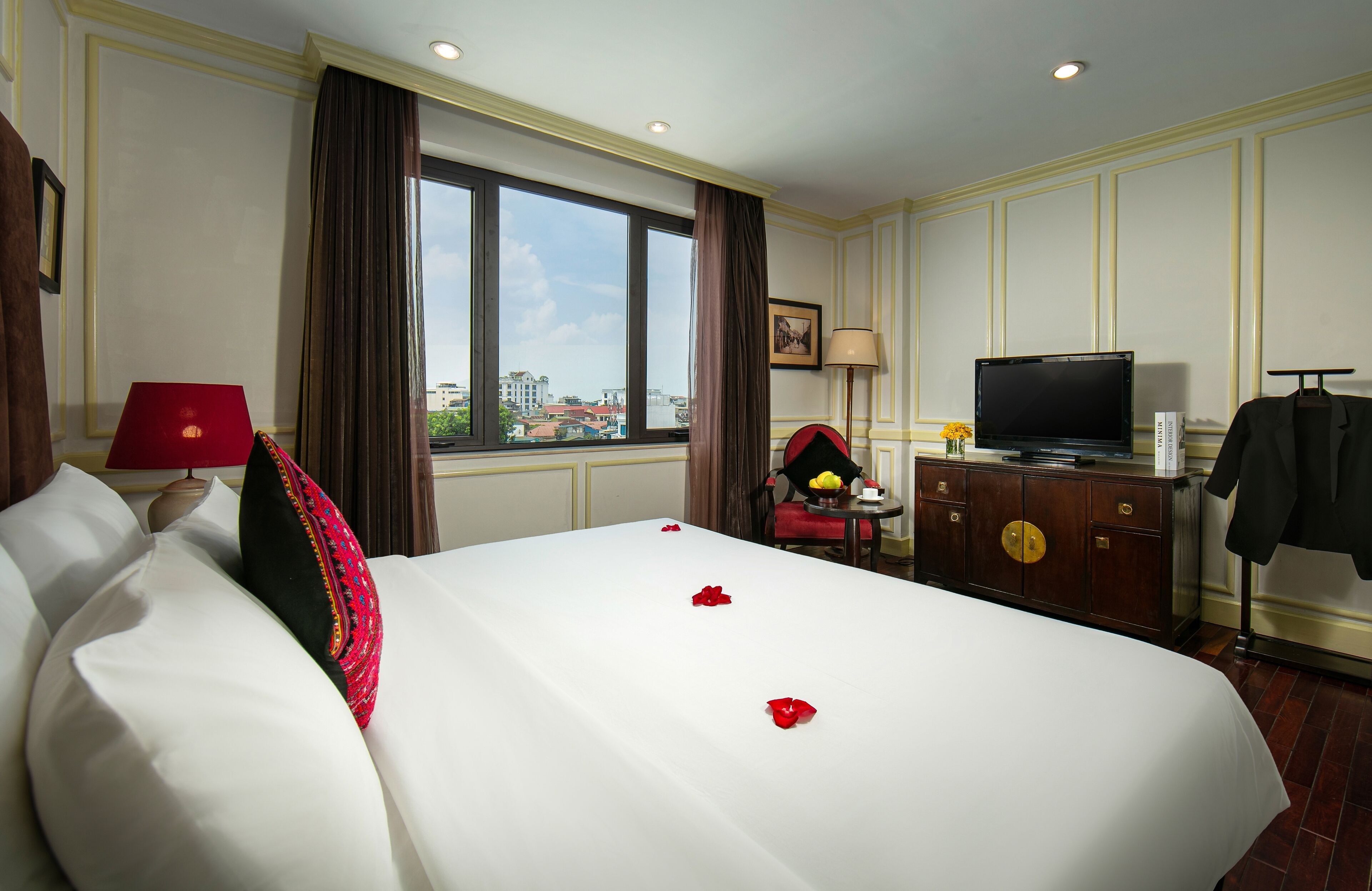 A hotel room with a large bed, a television, a dresser, and a view of the city through the window.