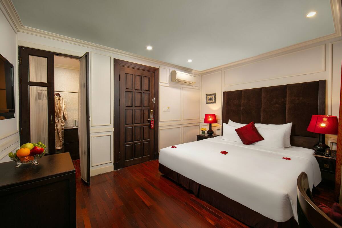 Una habitación de hotel con una cama grande, dos lámparas de noche, un aparador de madera y un frutero.