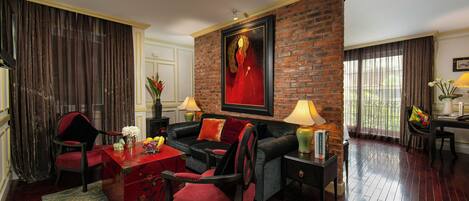 Una sala de estar con una pared de ladrillo, un sofá rojo, un sillón negro, una mesa de centro roja y una mesita auxiliar verde con una lámpara.