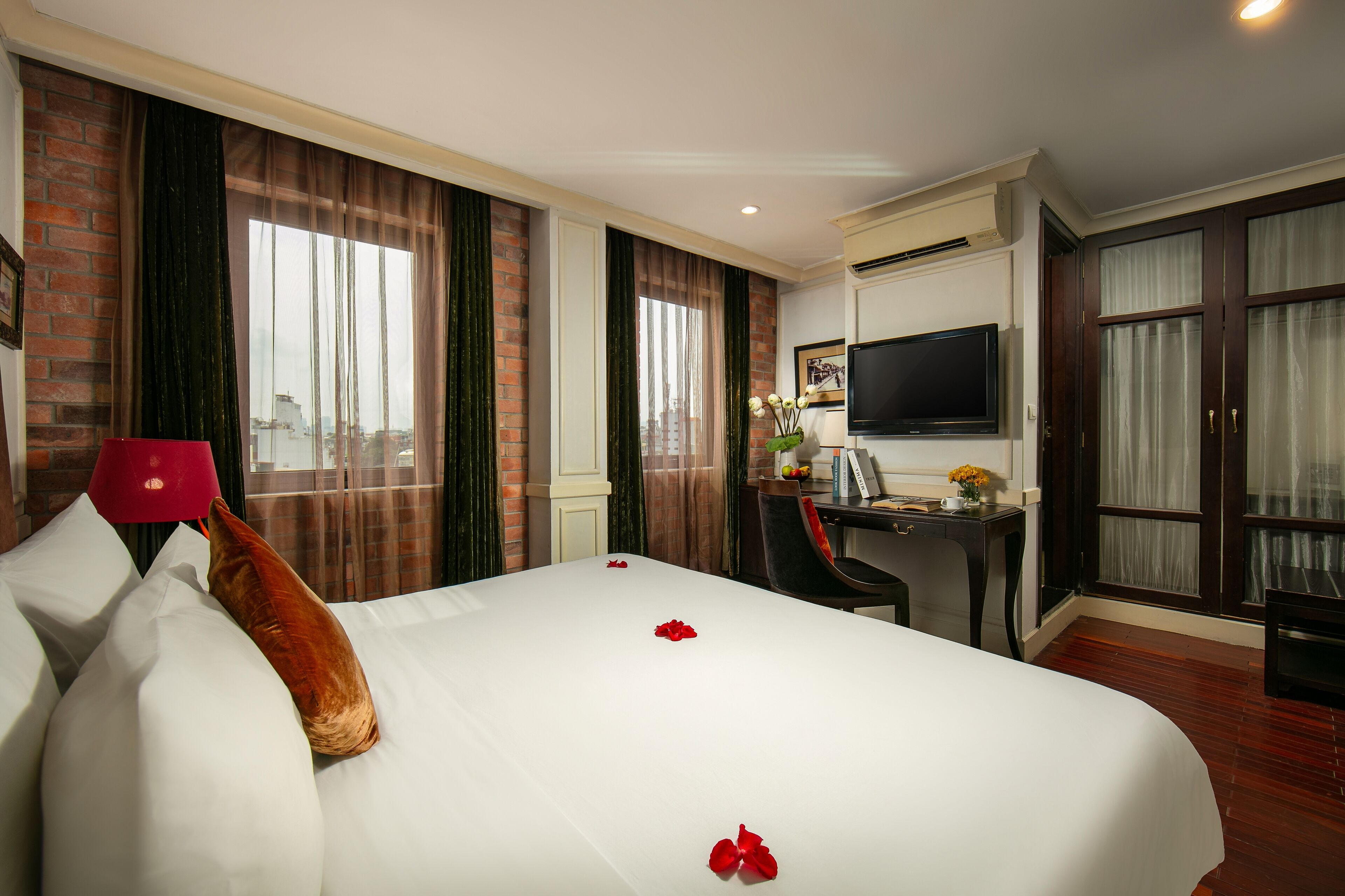 A hotel room with a large bed, a desk, a TV, and a view of the city.
