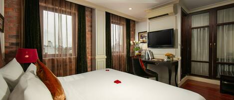 A hotel room with a large bed, a desk, a TV, and a view of the city.