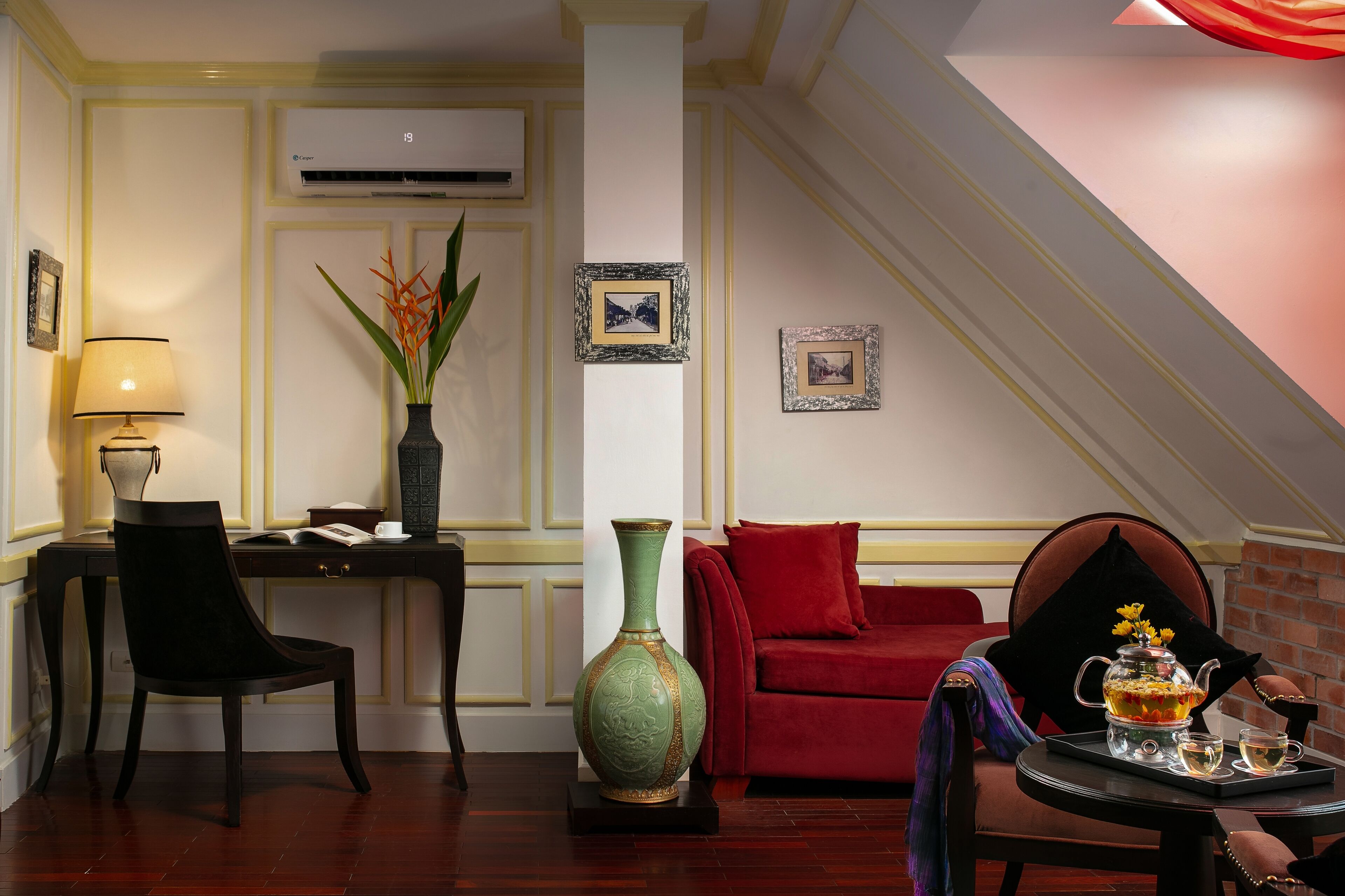 A room with a desk, chair, red sofa, and a table with a teapot and cups.