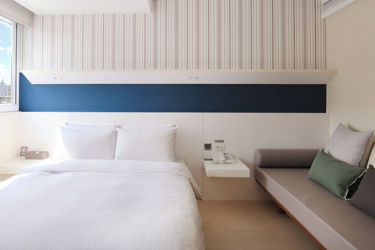 Habitación de hotel con cama, sofá, mesita de noche con teléfono y pared a rayas.