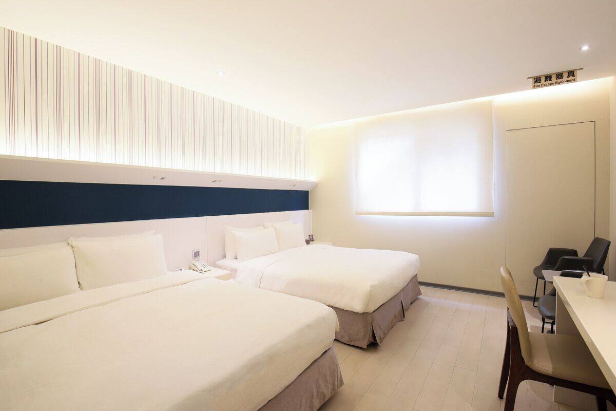A hotel room with two beds, a desk, and a window.