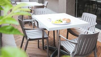 Un área de comedor al aire libre con mesas y sillas blancas, un plato de comida y una taza de café.