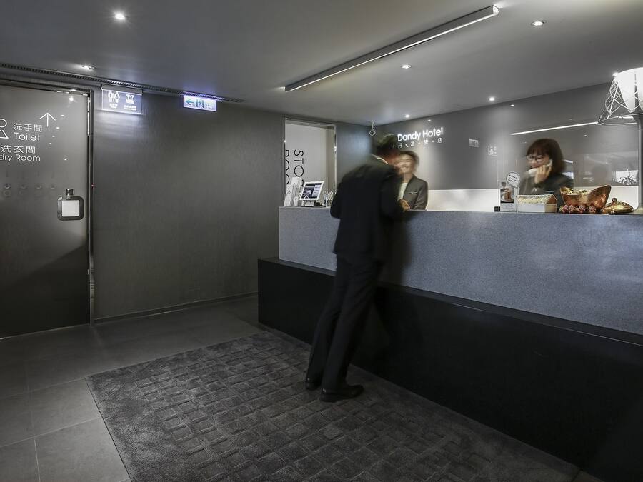 A hotel reception area with a reception desk, a digital screen, and directional signs for amenities like the toilet and laundry room.