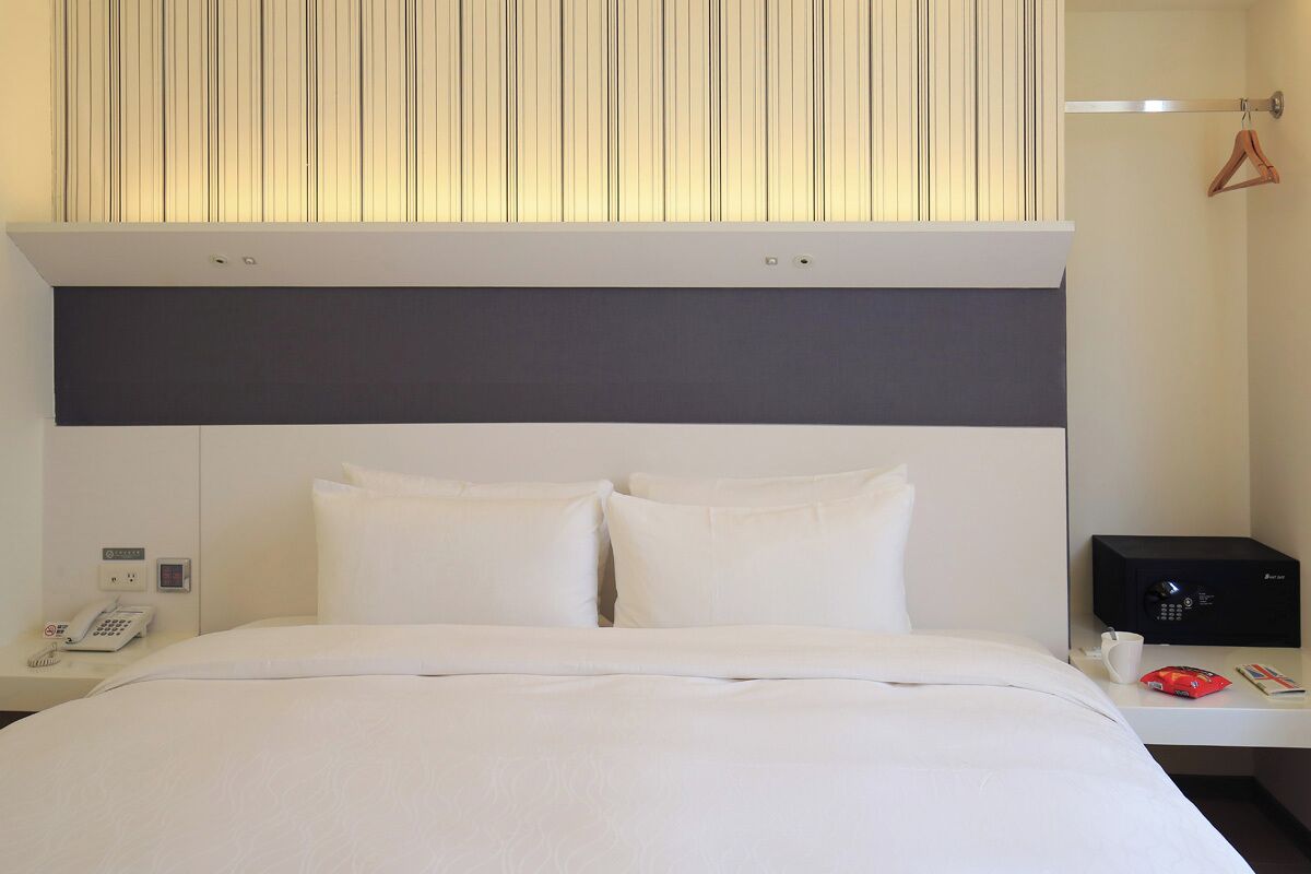 A hotel room with a bed, a bedside table with a phone, a microwave, and a hanging coat rack.