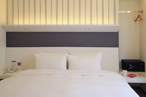 Een hotelkamer met een bed, een nachtkastje met een telefoon, een magnetron en een kapstok.