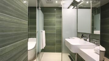Un baño moderno con cabina de ducha de vidrio, un lavamanos blanco y un inodoro.