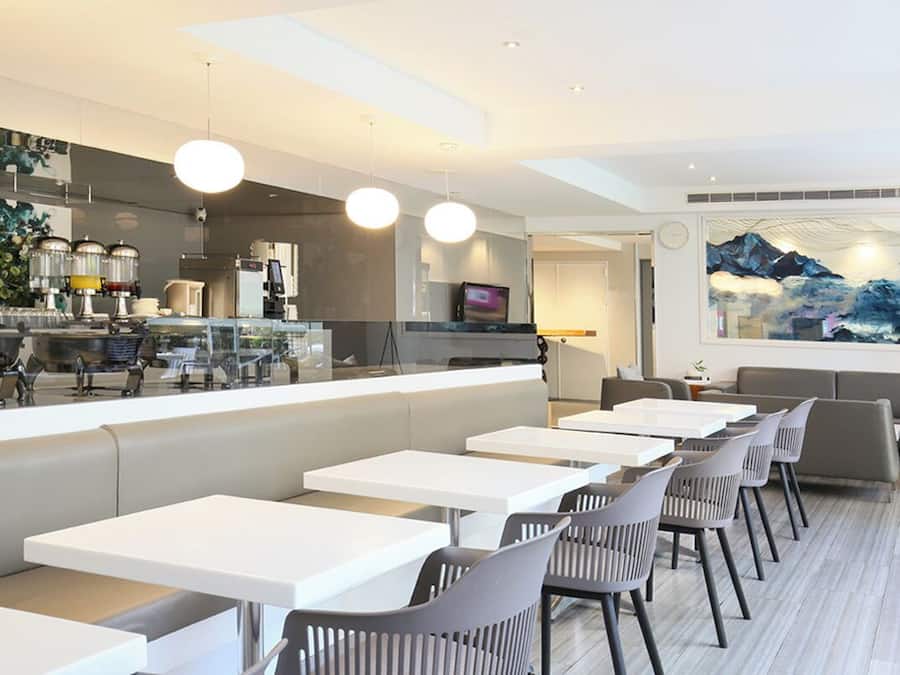 A modern restaurant with white tables and grey chairs, a bar area with a counter, and a large painting of a mountain landscape.